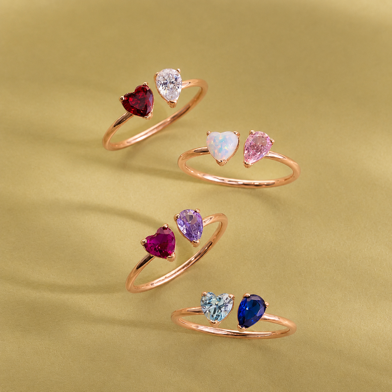Set of four rose gold rings with heart-shaped gemstones on a green background